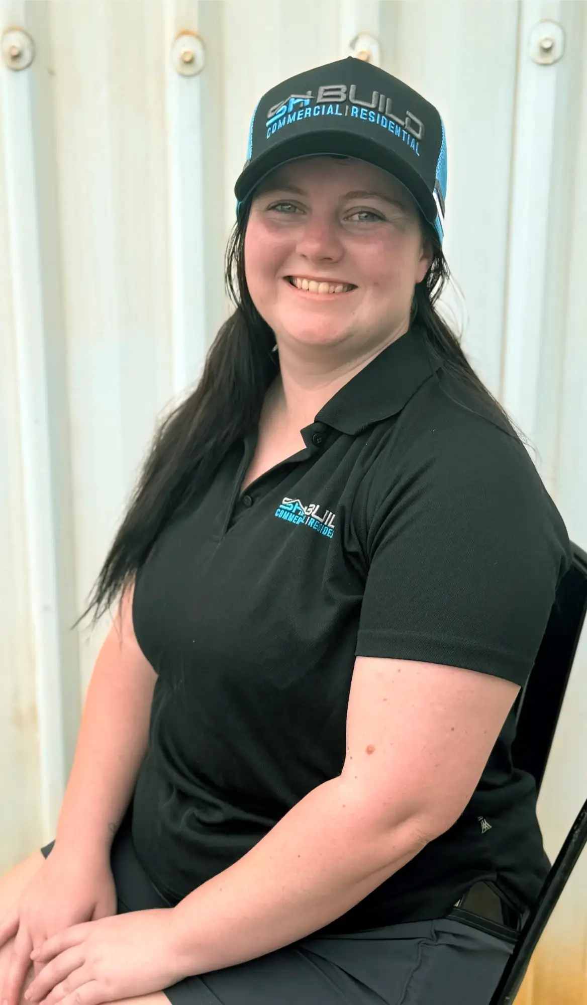 Smiling woman in black polo shirt and cap.
