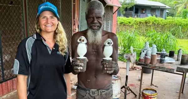 Two people holding painted owl sculptures outdoors